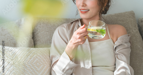 Photos A woman sits on a sofa and drinks lemon water, detox water.