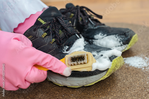 Closeup photo of man cleaning sneakers with special cleansing foam and brush. Scrubbing shoe toe with cleaning brush and foam
