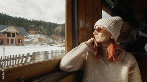 A woman rides on an old train in Romania. She looks out the window and enjoys the views of nature as the train travels along its path through the landscape.