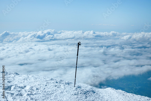 Canvas Print Lone trekking pole on snowy mountain summit above clouds respect nature concept