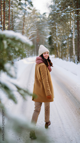 Playful young woman leading her romantic partner down a tranquil winter forest trail, looking back over her shoulder to encourage them to catch up.