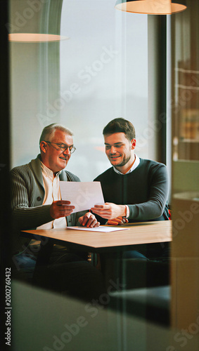 Retiring family business founder passing the torch to his millennial son while proudly reviewing their final succession agreement.