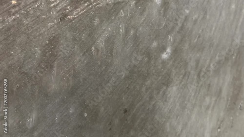 White ethereal smoke, vapor, or steam dissipating in a slow, gentle abstract motion over a dark, textured gray stone or concrete background with a subtle shimmer