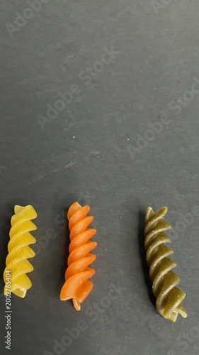 Colorful uncooked fusilli pasta spinning on a dark background. Variety of italian raw rotini pasta in green, yellow, and orange, showcasing healthy carbohydrates and italian cuisine