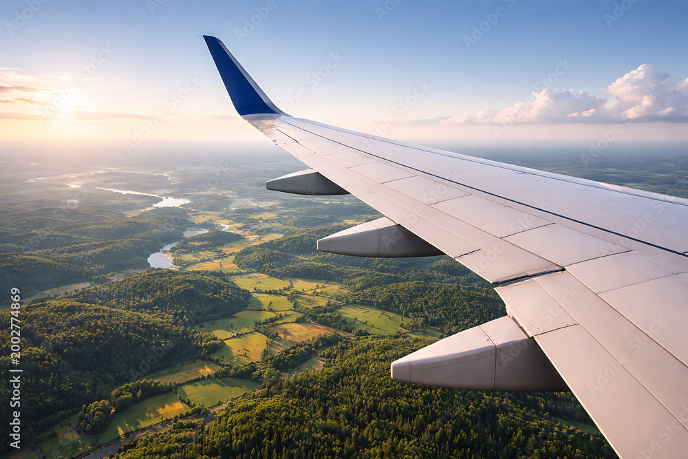 Obraz premium View from airplane window showing a commercial aircraft wing flying high above beautiful green countryside valleys and a winding river during a peaceful golden sunrise