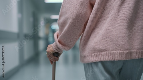 高齢の日本人女性が杖を使って歩いている後ろ姿。病院や介護施設でのリハビリやケアのシーンに適した素材。