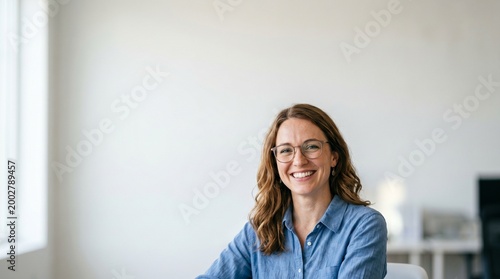 A smiling, middle-aged woman with glasses wearing a blue shirt in an office setting