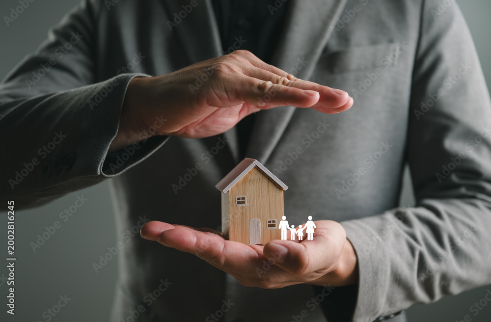 Naklejka premium Businessman hands protect wooden house model and family icon. Real estate insurance, home security, and financial property protection concept for mortgage loan, investment safety, and life assurance.