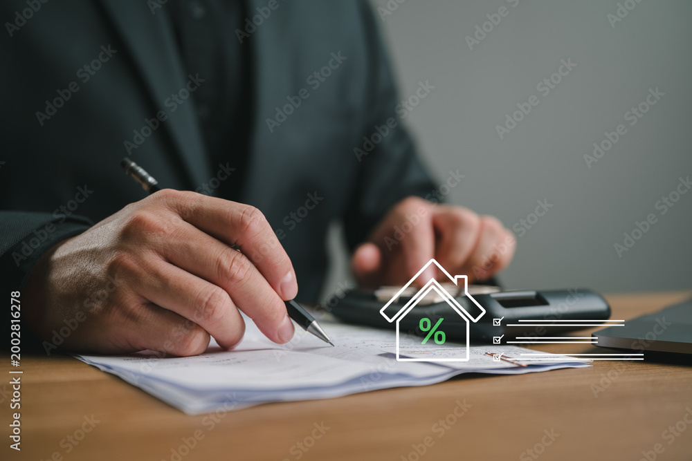 Obraz premium Businessman using calculator and writing on document with house interest rate icon. Concept of real estate tax, mortgage loan calculation, financial planning, and home property investment.