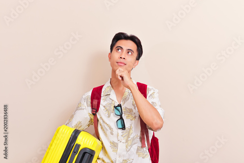Confused Asian traveler holding yellow suitcase and thinking about destination choices, flight booking complexity, or travel insurance options.