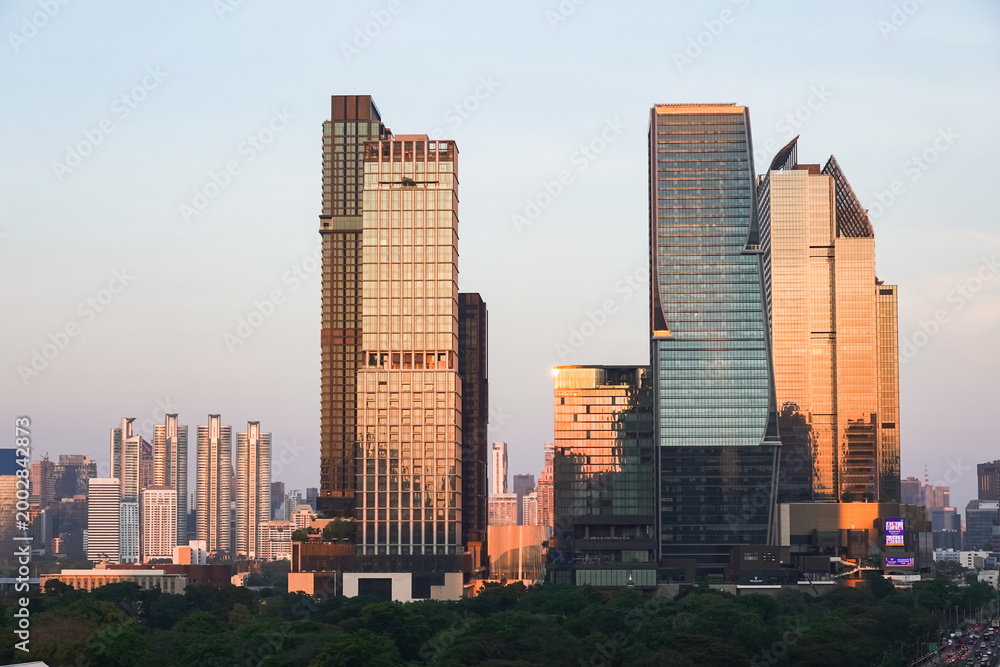 Fototapeta premium An aerial view from Dusit Central Park in the evening, a favorite landmark for tourists and travelers. The sunset casts its light reflecting off the tall buildings surrounding Lumpini Park
