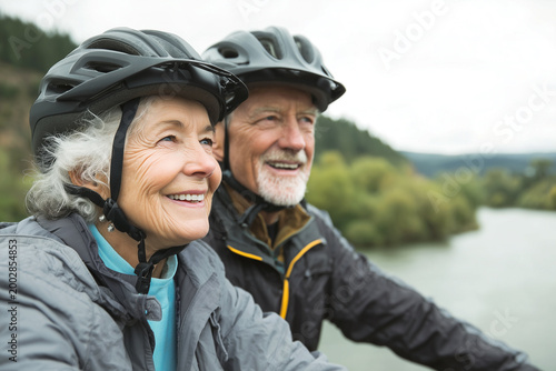 Pareja de adultos mayores realizando bicicleta al aire libre en un entorno natural. Dos adultos mayores avanzan con cascos y ropa deportiva, mostrando vitalidad, motivación y un estilo de vida 