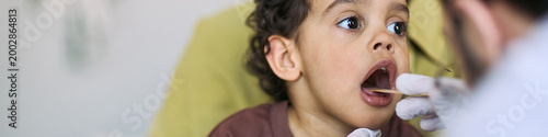 фотографія Website banner of child opening mouth during throat examination by doctor, showi