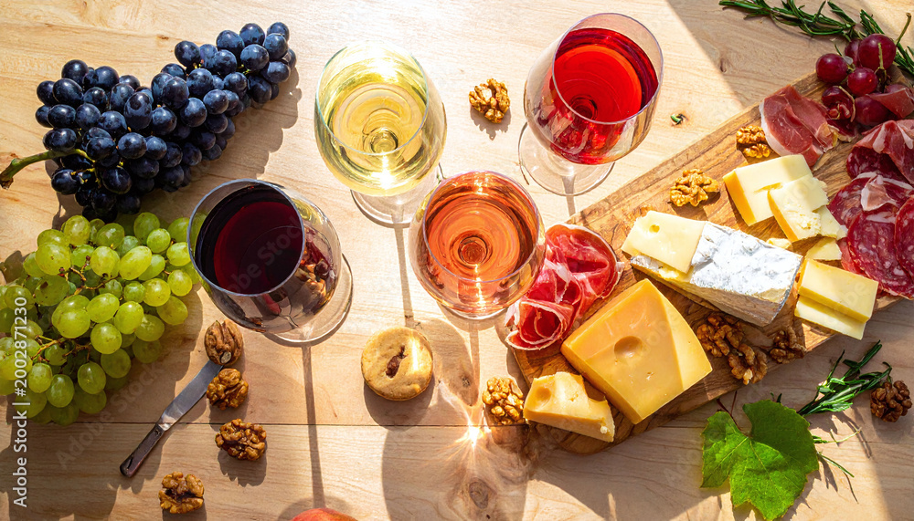 Fototapeta premium Elegant wine tasting scene featuring red, white, and rose glasses, paired with gourmet cheeses, cured meats, and fresh grapes. Perfect for upscale lifestyle and hospitality branding.