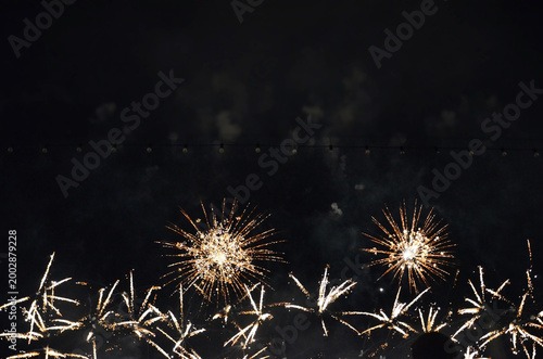 Brilliant golden fireworks burst against the dark night sky, creating a dazzling display of light and sparkles