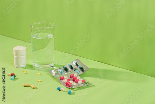 Fotografía Medication pills, capsules, and glass of water on green background