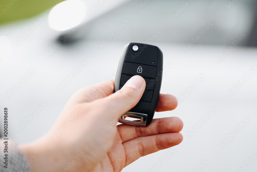 Fototapeta premium black car keys in woman hand, close-up view, white car in background, opening or closing car with signalization or alarm system, car theft, carjacking, car safety concept, selective focus
