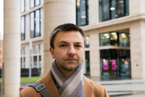 Man lawyer standing near modern office building. Serious male face with expression of confidence and restraint. Successful professional portrait in urban environment for business concept.