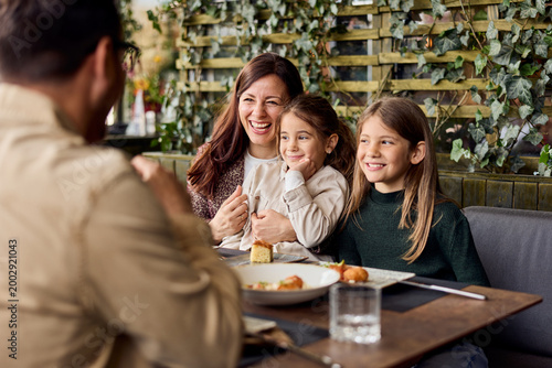 Happy Mother and Two Daughters Laughing Together at Restaurant Family Dining and Bonding Moment