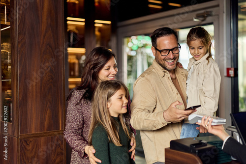 Happy Family Making Mobile Payment at Cafe Checkout, Parents With Two Children Smiling Together