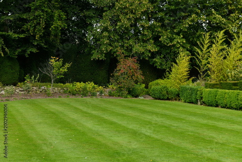 Manicured green lawn with prominent stripes bordered by lush trees and landscaped hedges in a formal English garden