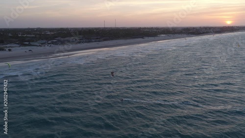 Preá Beach in Cruz Ceará Brazil shows multiple kitesurfers riding steady trade winds on Atlantic Ocean near sandy shoreline at sunset with village in background, aerial wide drone shot