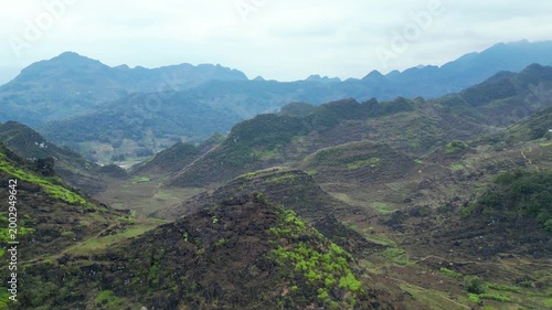 Panoramic drone view of rolling karst hills with terraced slopes and deep valleys under expansive hazy sky in Dong Van Karst Plateau Geopark Ha Giang Northern Vietnam