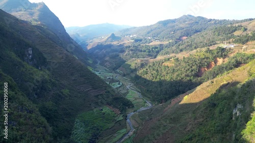 Aerial drone shot of winding road snaking through rocky terraced valley with river below under hazy sky in Dong Van Karst Plateau Geopark Ha Giang Northern Vietnam