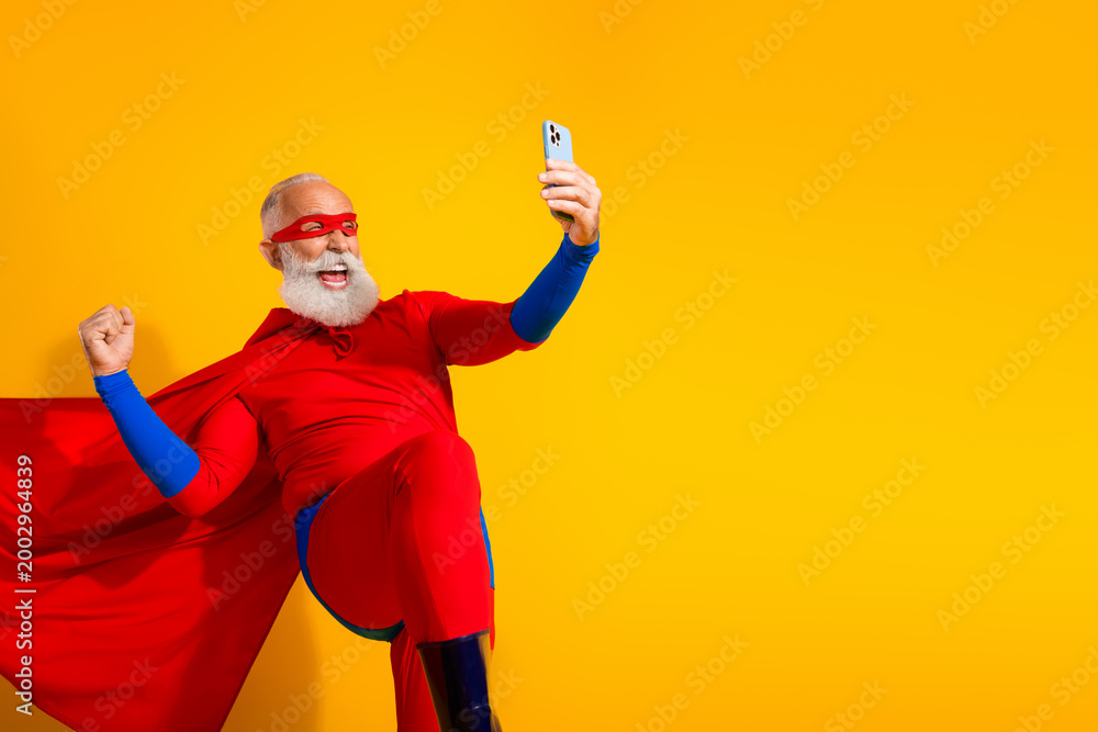 Fototapeta premium Energetic senior superhero in bright red costume strikes a dynamic pose as he selfies against a yellow background