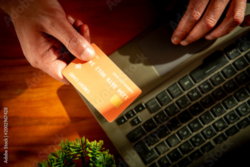 Cuadro en lienzo High angle close up of male hands holding an orange credit card while using a laptop keyboard for digital transaction and online shopping