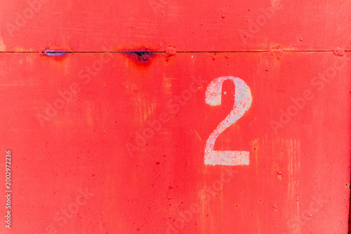 Konstfotografi Number 2 stenciled on red painted metal surface with rivets