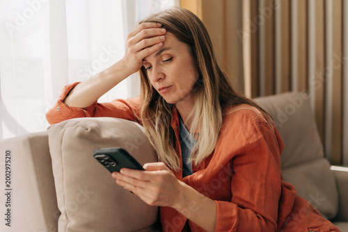 Fotografie Upset anxious woman sitting on the sofa and looking at her mobile phone