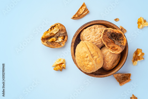 Walnuts in wooden bowl with cracked walnuts on blue background, healty snack, top view