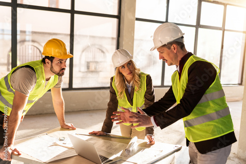 Workers discuss project plans in construction site during daylight with clear view of windows