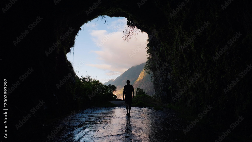 Fototapeta premium Person walking out of dark cave tunnel