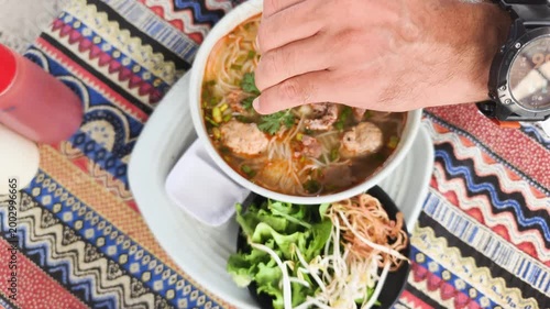 Authentic Bun Bo Hue captures hand squeezing fresh lime into spicy beef noodle soup. Vibrant greens and aromatic broth highlight traditional Vietnamese flavors. This authentic Bun Bo Hue meal.