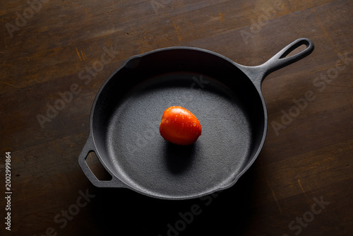 Top view of skillet with red tomato on wooden background