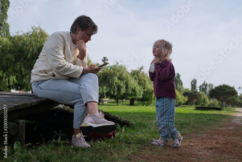 Seeking Attention: Toddler Girl Trying to Distract Her Mother from Smartphone in the Park