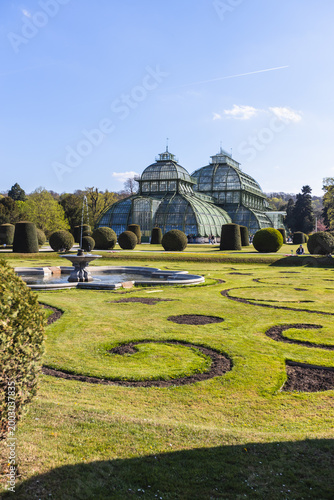 Canvas Print Palmenhaus Schönbrunn in Vienna, Austria, featuring ornate glass and metal greenhouse architecture with formal landscaped gardens and fountain under clear blue sky