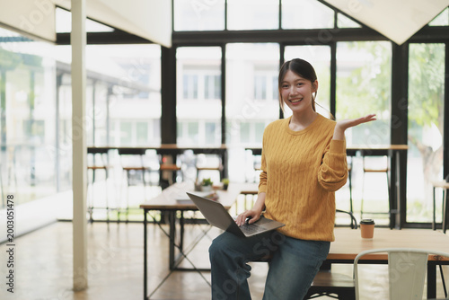 Asian businesswoman freelancer smiling and presenting with open hand, working in a modern coworking office space, concept of entrepreneurship and digital nomad lifestyle Free Download Asian businesswoman freelancer smiling and presenting with open hand, working in a modern coworking office space, concept of entrepreneurship and digital nomad lifestyle - GFXLoad