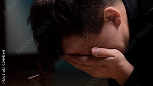 Canvas Print Man covering his face with hand, deeply distraught while praying beside a small