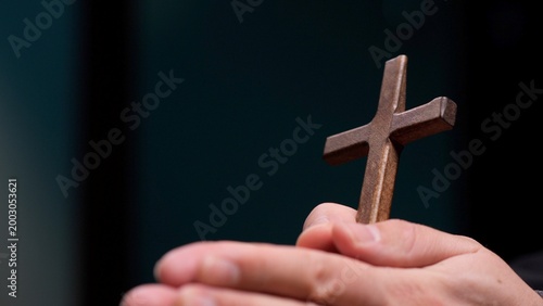 Photography Hands clasping a small wooden cross in prayer, evoking faith, hope and quiet dev