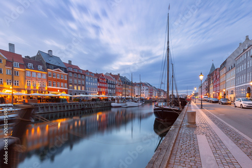 Quiet Nyhavn waterfront at dawn with moored boats, calm canal reflections, and soft early morning light in Copenhagen, Denmark.