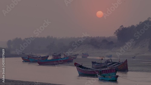 Colorful fishing boats anchored on a calm river beach at sunset with misty shoreline