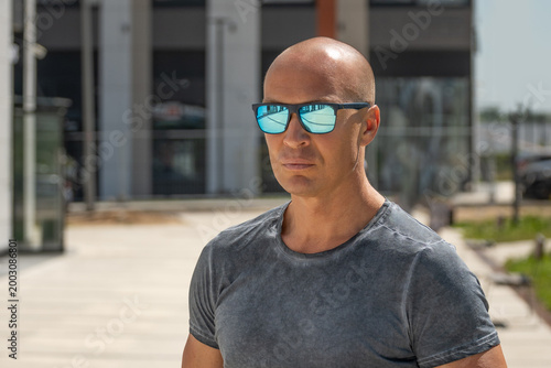 Confident bald man in sunglasses outdoor business portrait, strong leadership mindset and success concept, urban lifestyle, focus and decision making, copy space