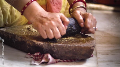 Indian Woman Grinding Spices on Traditional sil batta or Stone Grinder in Kitchen.	