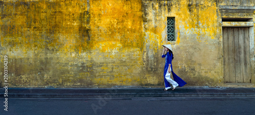 Bild auf Leinwand Vietnamese woman in traditional Vietnamese costume  walks along the walls of a traditional yellow house in Hoi An, Vietnam
