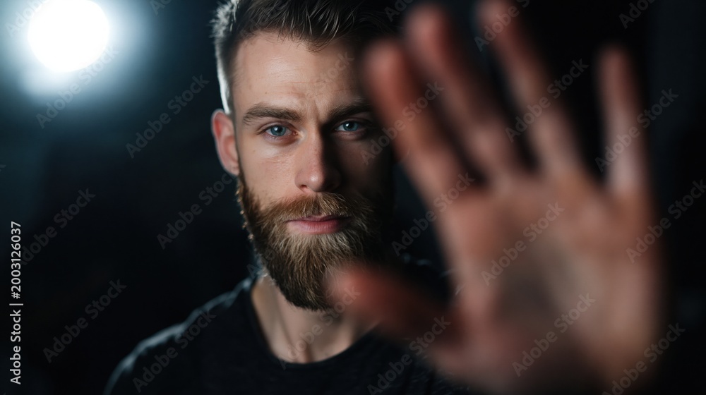 Fototapeta premium A man s hand is raised in a stop gesture, blocking the view of his face, symbolizing privacy, refusal, or a boundary. This composition conveys a sense of seriousness and protection.