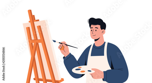 Talented male artist in an apron holds a paint palette and brush while working on a new masterpiece on a wooden easel.
