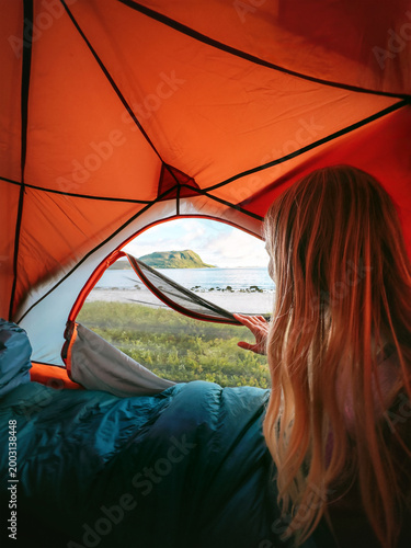 Woman inside tent looking at the view from the entrance - travel lifestyle summer camping vacations outdoor, tourist girl solo on adventure trip weekend getaway in the wild